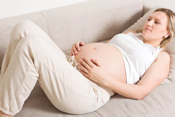 Těhotná žena sedí na pohovce — Stock fotografie