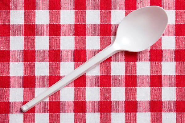 Plastic spoon on checkered tablecloth — Stock Photo, Image