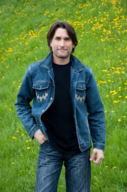 The dark-haired man in jeans on a meadow clipart