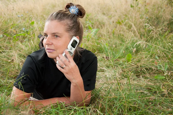 Mujer de mediana edad con el teléfono tumbado en un prado — Foto de Stock