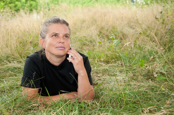 풀밭에 누워 전화를 가진 중 년 여성 — 스톡 사진