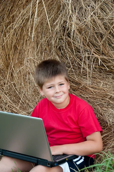En pojke med en laptop i fältet — Stockfoto