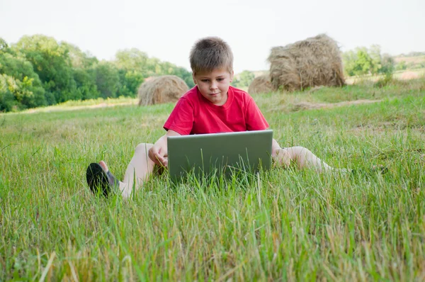 Мальчик с ноутбуком в поле — стоковое фото