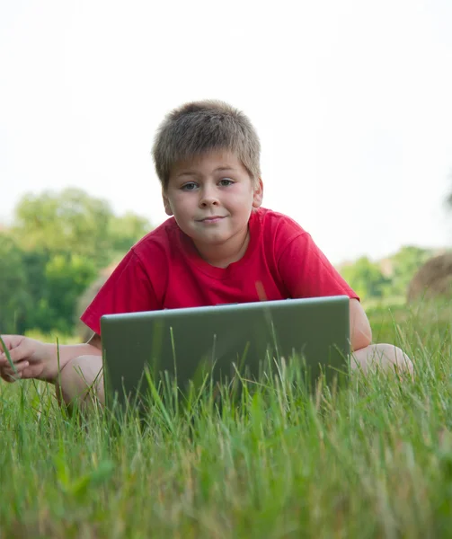 En pojke med en laptop i fältet — Stock fotografie