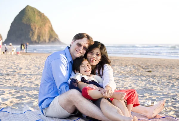 Маленькая семья с маленьким мальчиком-инвалидом, сидящим на пляже рядом — стоковое фото