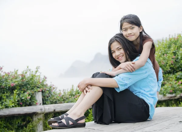 Dos chicas sentadas juntas cerca de un mar brumoso en el fondo —  Fotos de Stock