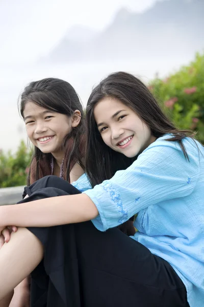Zwei Mädchen, die zusammen in der Nähe eines nebligen Ozeans im Hintergrund sitzen — Stockfoto