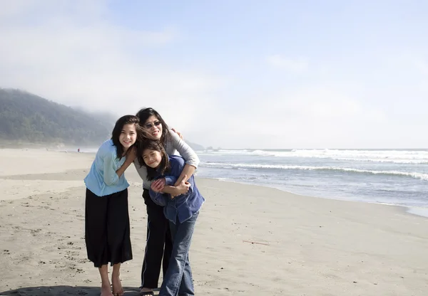 Aziatische moeder en twee dochters lachend op het strand door zee. — Stockfoto