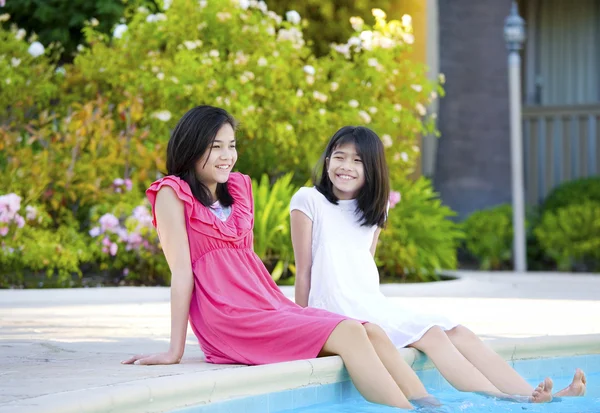 Zwei junge Mädchen, die am Pool sitzen und lächeln — Stockfoto