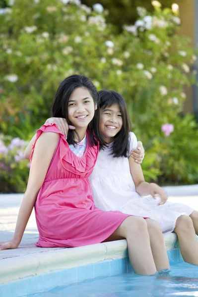 Dos chicas jóvenes sentadas junto a la piscina, sonriendo —  Fotos de Stock