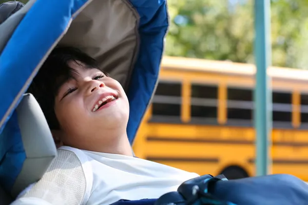 Deficiente menino de cinco anos em cadeira de rodas ao ar livre por ônibus escolar — Fotografia de Stock