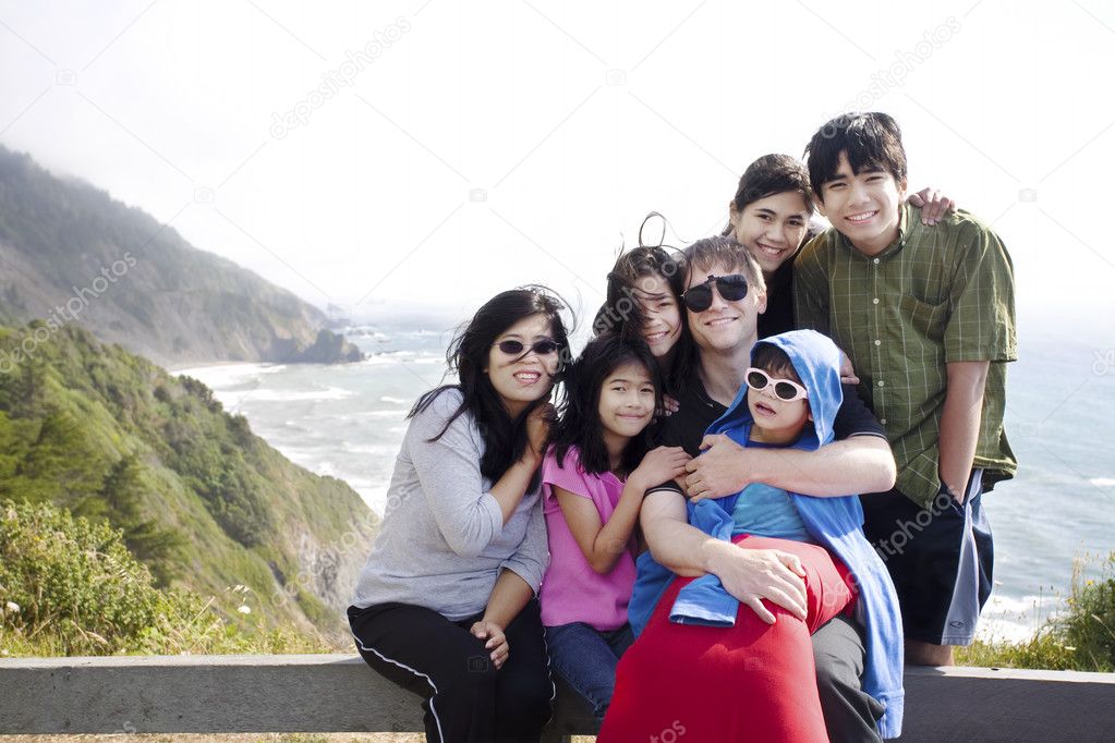 Multiracial family of seven sitting by the Pacific Ocean. Little