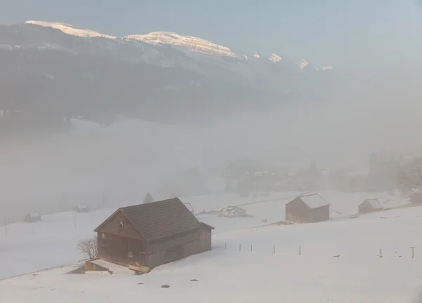 N cabañas en niebla con cimas de montaña sobresaliendo —  Fotos de Stock