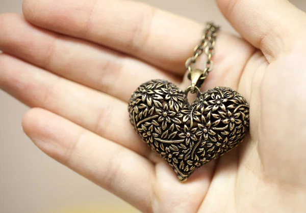 Подвеска в форме сердца, бронзового цвета с цепью в руке — стоковое фото