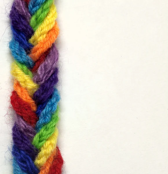 Шерстяные пряжи разных цветов, сотканные в плетеную косу, на белом фоне — стоковое фото