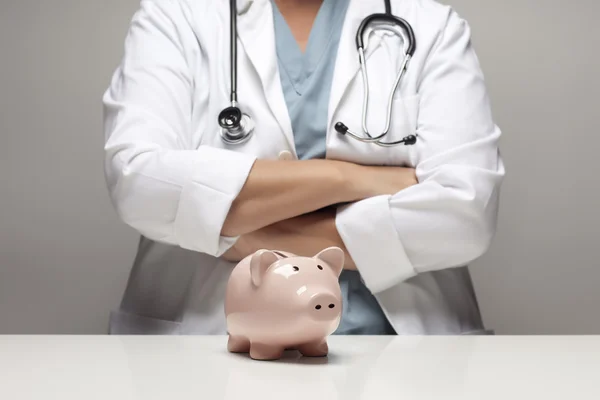 Arzt mit verschränkten Armen hinter Sparschwein — Stockfoto