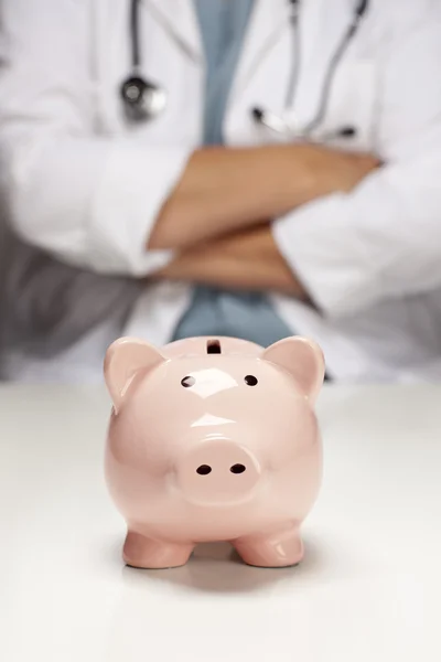 Arzt mit verschränkten Armen hinter Sparschwein — Stockfoto