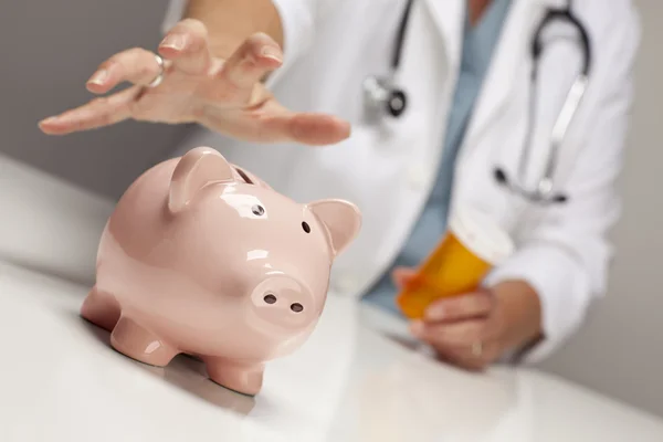 Doctor with Medicine Bottles Reaches for Piggy Bank. — Stock Photo, Image
