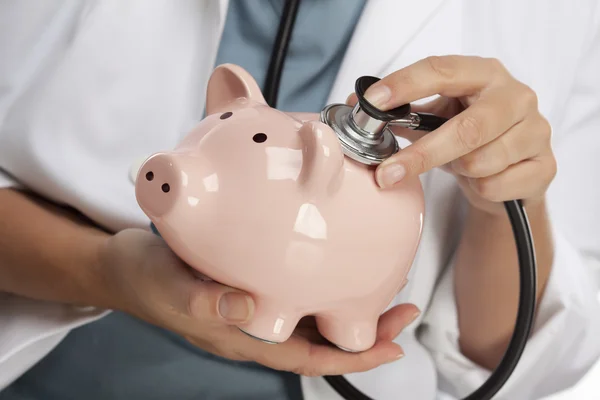 Arzt hält Stethoskop an Sparschwein — Stockfoto