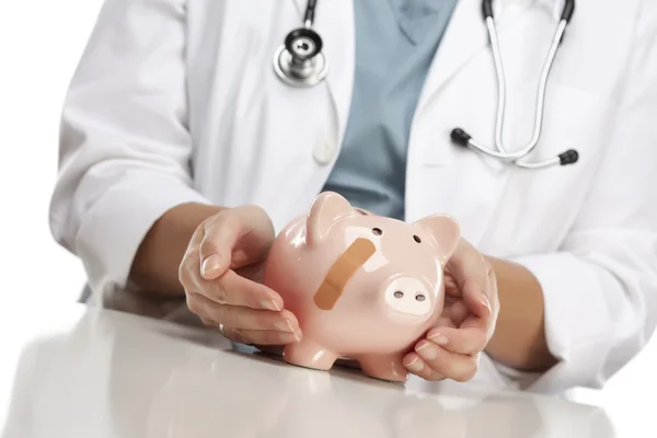 Médico Segurando as mãos carinhosas em um Piggy Bank com bandagem — Fotografia de Stock