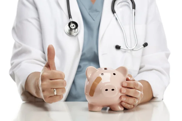 Arzt mit erhobenem Daumen hält Hand an bandagiertem Sparschwein — Stockfoto