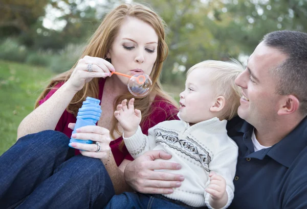 Padres jóvenes que soplan burbujas con su hijo en el parque —  Fotos de Stock
