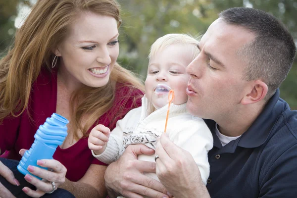 Giovani genitori soffiano bolle con il loro bambino nel parco — Foto Stock