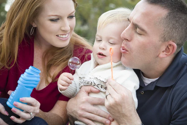 Молоді батьки дме бульбашки з їх дитиною хлопчика в парку — стокове фото
