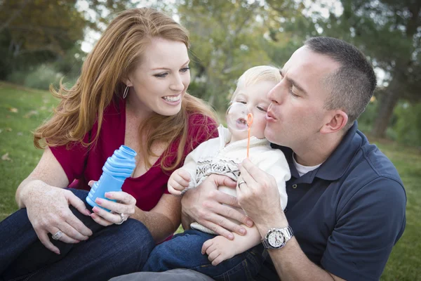 Jovens pais soprando bolhas com seu filho no parque — Fotografia de Stock
