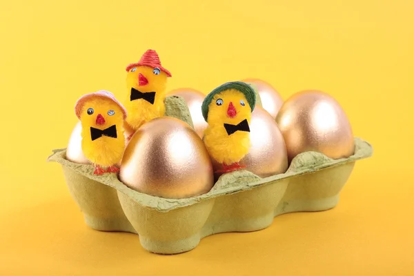 Golden Easter eggs and chicks in carton over yellow — Stock Photo, Image