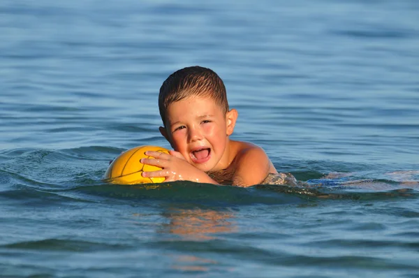 Мальчик с мячом в море — стоковое фото