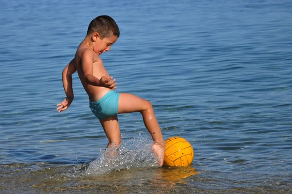 Chico pateando una pelota en el agua — Foto de Stock