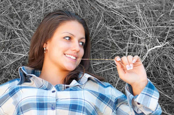 Beautiful young women lies on the pile of hay and smiles. — Stock Photo, Image
