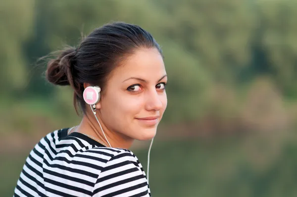 สาววัยรุ่นที่ยิ้มสวยฟังเพลงในขณะที่เพลิดเพลินกับธรรมชาติฤดูใบไม้ร่วง . — ภาพถ่ายสต็อก