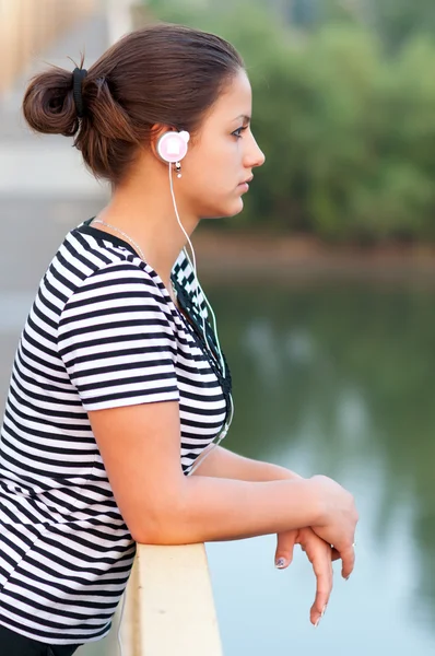 Junges attraktives Mädchen hört Musik, während es auf der Brücke steht. — Stockfoto