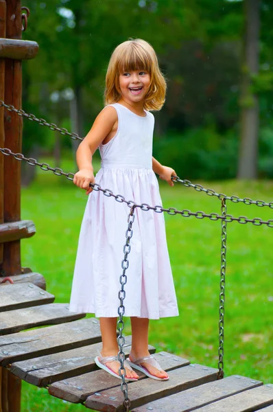 Beautiful little girl smiles while standing on the small wooden hanging bri — Stock Photo, Image