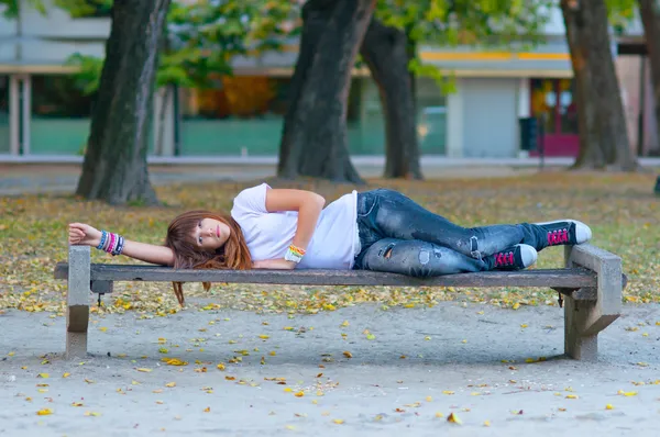 Teenage girl lies on the bench in the park on cloudy autumn day. — Stock Photo, Image
