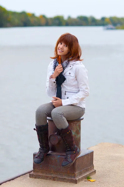 美丽微笑的红发少女坐在码头上多云的列上 — 图库照片