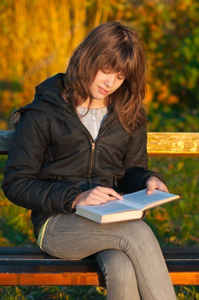 Bella ragazza adolescente legge il libro nel parco nella soleggiata giornata autunnale — Foto Stock