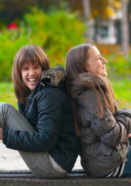 Pretty teenage girls laughing and joking while sitting in the park clipart