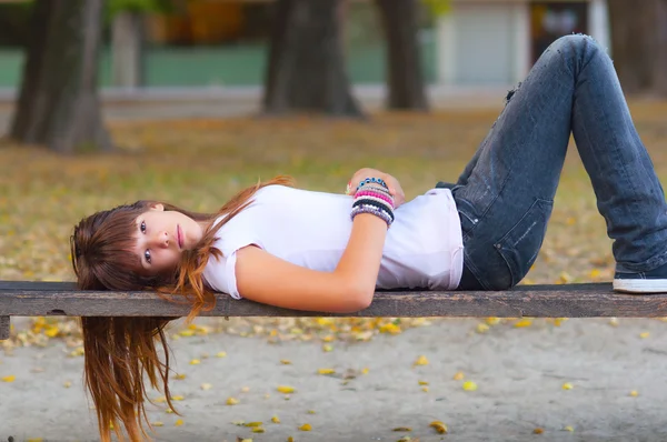 Bastante adolescente acostada en el banco en el parque — Foto de Stock