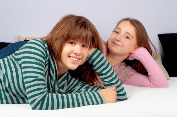 Dwie całkiem nastoletnich dziewcząt, leżąc na łóżku i uśmiechając się — Zdjęcie stockowe