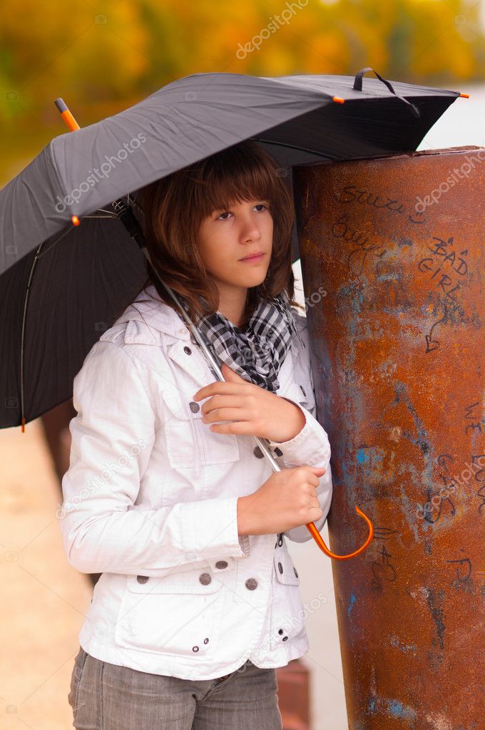 Beautiful sad teenage girl holds umbrella on cloudy autumn day