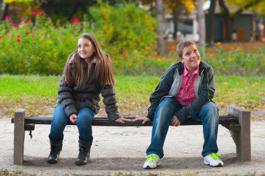 Shy boy and the girl sitting in the park and lightly touching each other fi clipart