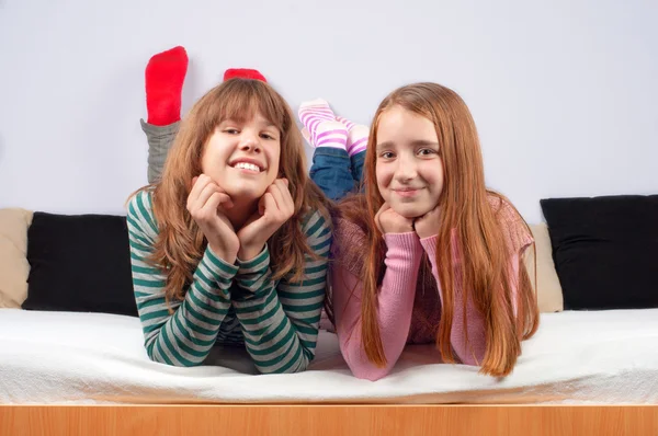 Zwei hübsche Mädchen im Teenageralter liegen auf dem Bett und lächeln. — Stockfoto