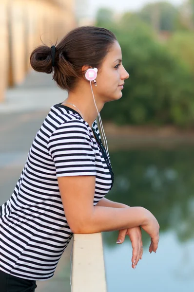 Fiatal, vonzó lány a hídon állva zenét hallgatni — Stock Fotó