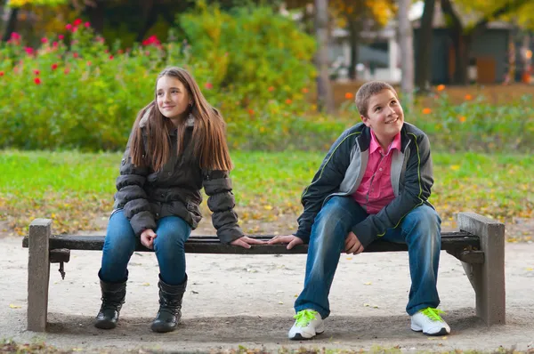 Tímido menino e a menina sentados no parque e levemente tocando uns aos outros fi — Fotografia de Stock