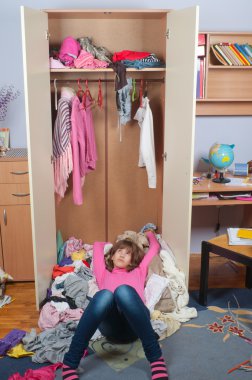 Untidy teenage girl lying on pile of wrinkled clothes inside her wardrobe clipart