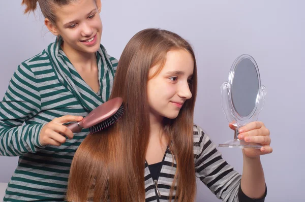 Pretty teenage girls combing hair and watching themselves in mirror — Stock Photo, Image