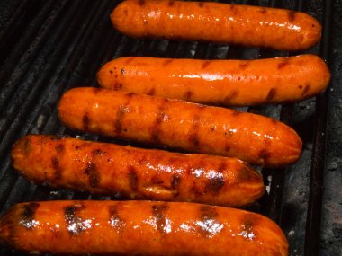 A row of five hotdogs on a bbq grill clipart
